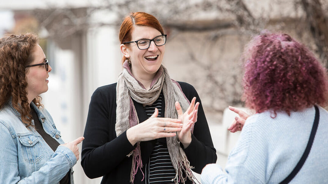 Three women are smiling as they have a friendly conversation using Auslan.